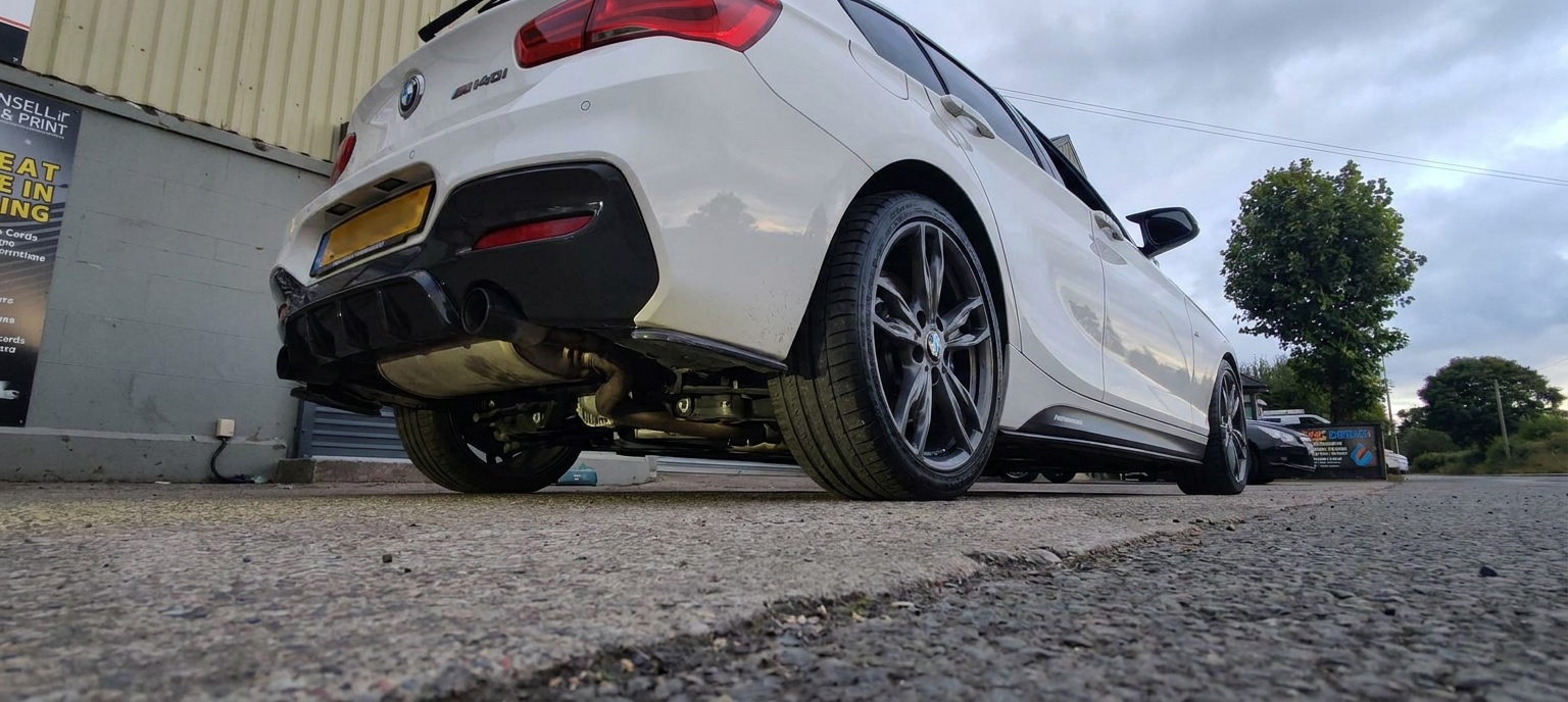 Low angle rear view of a white BMW M140i showing the tinted rear screen and quarter glass